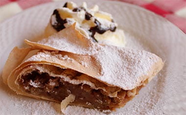 Hungarian apple strudel with cream, dusted with icing sugar, on a plate